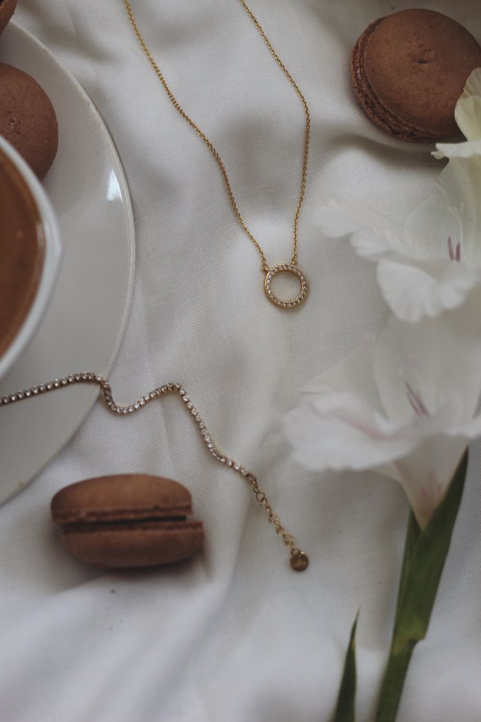 Top view of macarons, jewelry, and white flowers on elegant fabric.
